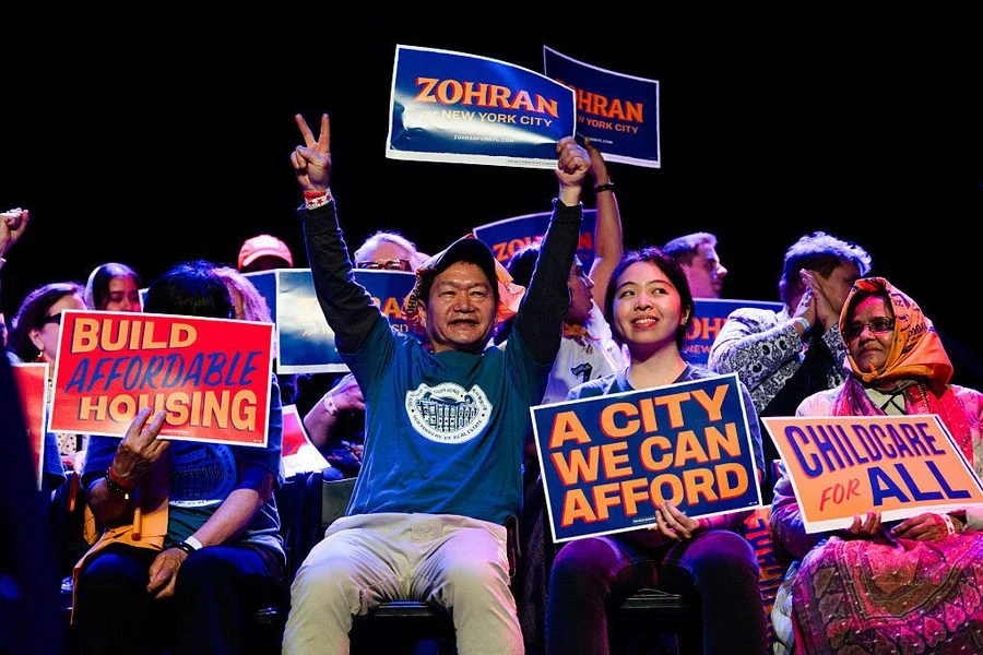 Semangat perjuangan Zohran Mamdani terpancar dari antusiasme para pendukungnya yang membawa pesan-pesan penting: 'Build Affordable Housing', 'A City We Can Afford', dan 'Childcare for All'. Kredit: Common Dreams.